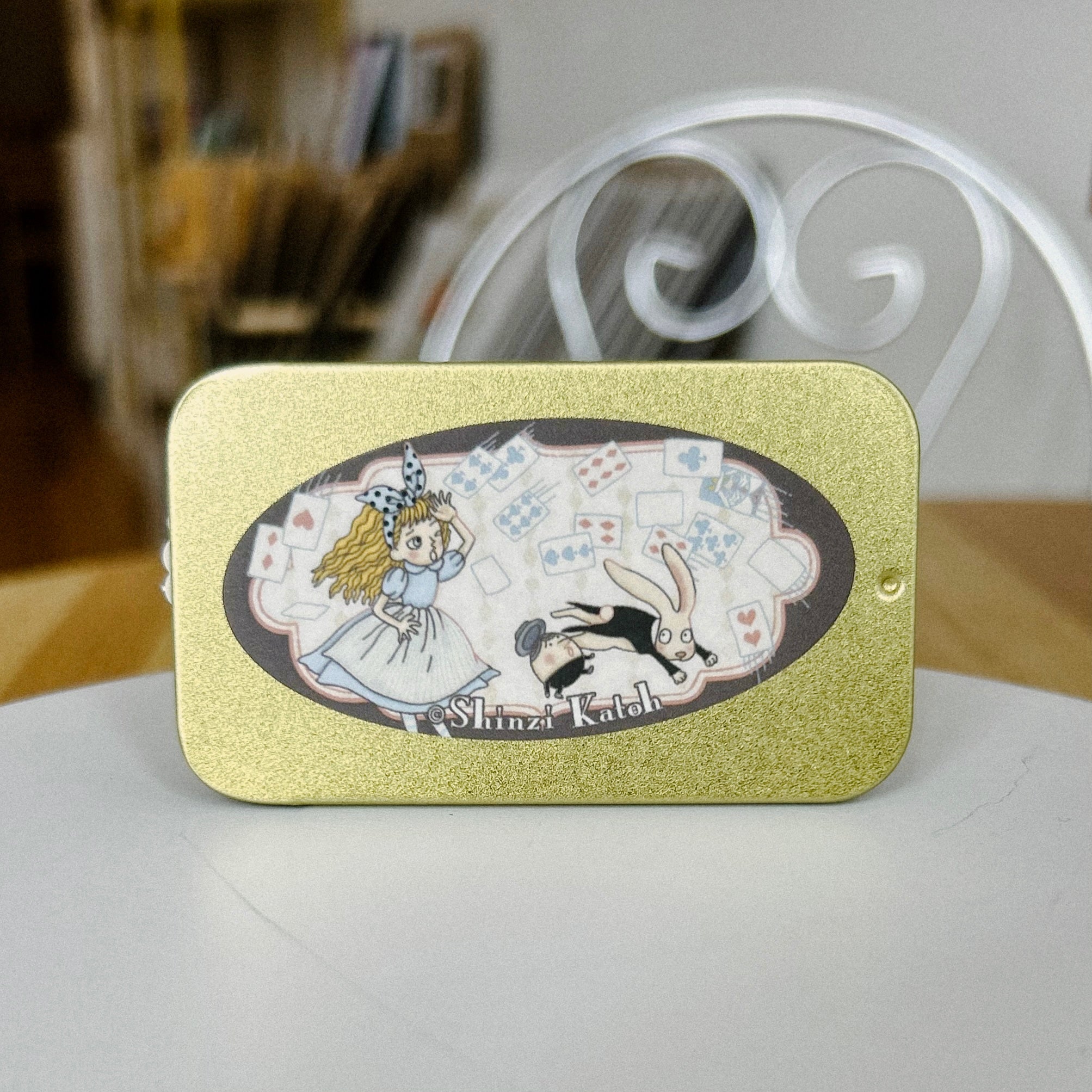 Decorative tin with illustrations of Alice and a rabbit on a gold background